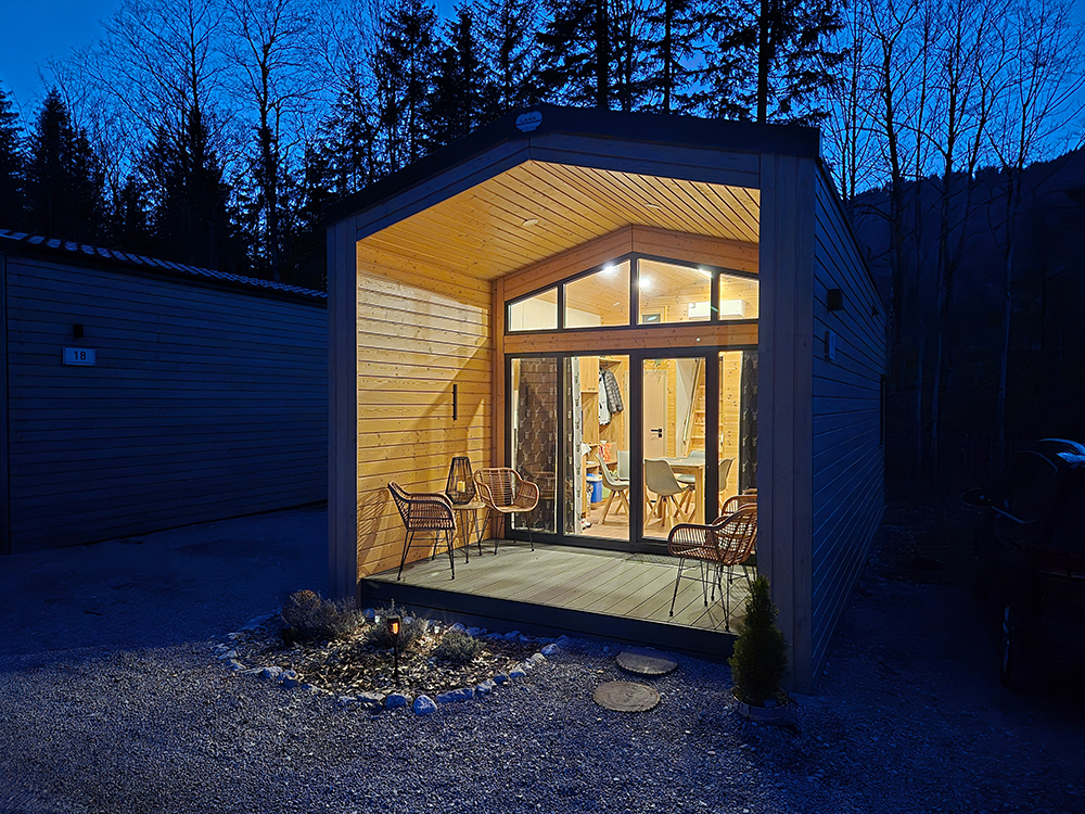 Aussenansicht des Alpenchalet Wendelsteins in der blauen Stunde, also in sternenklarer Nacht, stillvoll, romantisch und einladden beleuchtet. Durch das Panoramafenster leuchtet das stillvolle Licht und zeigt den gemütlichen Innenraum des Chalets und lädt zum entspannen und erholen ein.