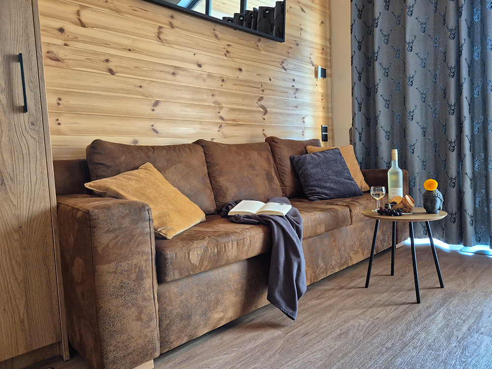 Gemütliches Sofa im Alpenchalet Wendelstein mit direktem Blick aus dem Panoramafenster auf die Berge Aiplspitz und Jägerkamp – perfekt für entspannte Abende in der Urlaubsregion Tegernsee Schliersee.